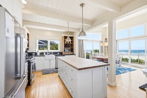 A modern kitchen with a large island, stainless steel appliances, and a view of the ocean.