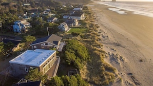 Vue aérienne d’un quartier résidentiel situé sur la côte, avec des maisons jouxtant une plage. On y voit un mélange de bâtiments à un ou plusieurs étages, dont certains sont dotés de balcons apparents.