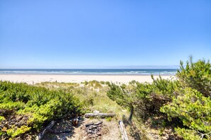 A beach view with sand, sea, and sparse vegetation.