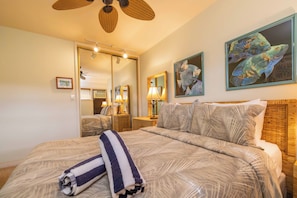 A hotel room with a bed, a mirror, a wall-mounted fish painting, and a ceiling fan.