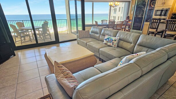 A spacious living room with a large sofa, a coffee table, and a view of the ocean through large sliding glass doors.