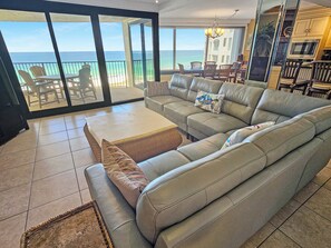 A spacious living room with a large sofa, a coffee table, and a view of the ocean through large sliding glass doors.