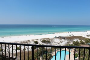 Blick auf den Strand vom Balkon mit Pool, Strandliegen und einem Rettungsturm.