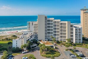 A hotel with multiple floors, a parking area, and a beach view.