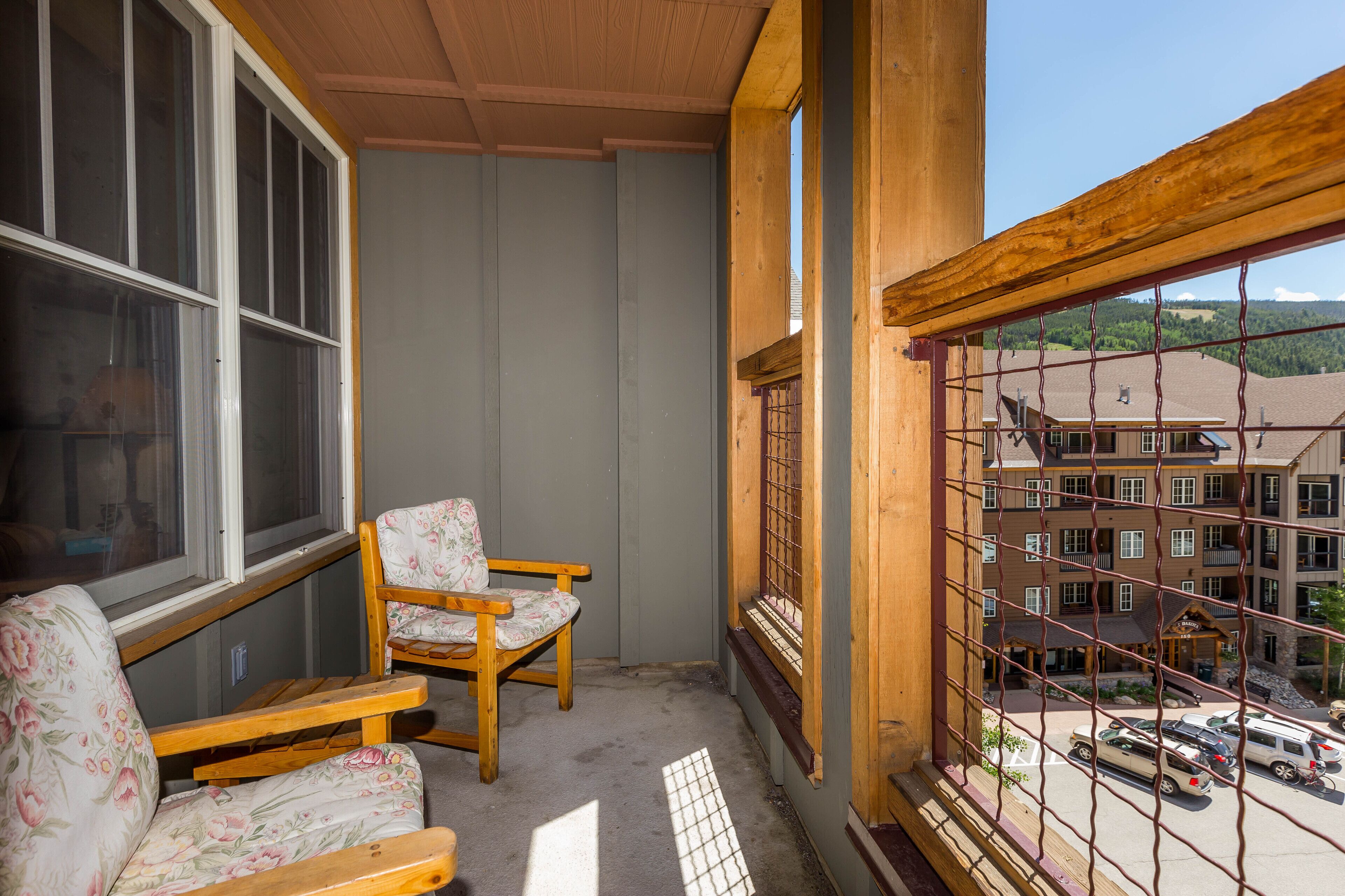 Un balcon avec des chaises en bois, une vue sur un parking et, au fond, un immeuble avec de nombreuses fenêtres.