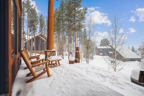 Escape to a serene cabin surrounded by a winter wonderland, featuring a cozy porch and a warm stone fireplace.