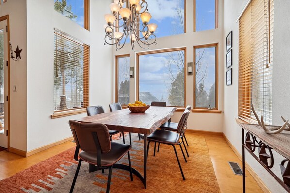 Enjoy meals in this dining area with a large table and six chairs, surrounded by large windows and a decorative chandelier.