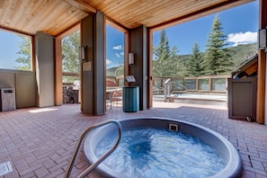 A hot tub with a wooden deck, outdoor seating, and a view of trees and mountains.