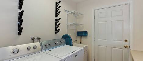 Une buanderie équipée d’un lave-linge et d’un sèche-linge à chargement frontal, d’une chaise bleue et d’une porte dotée d’une poignée.