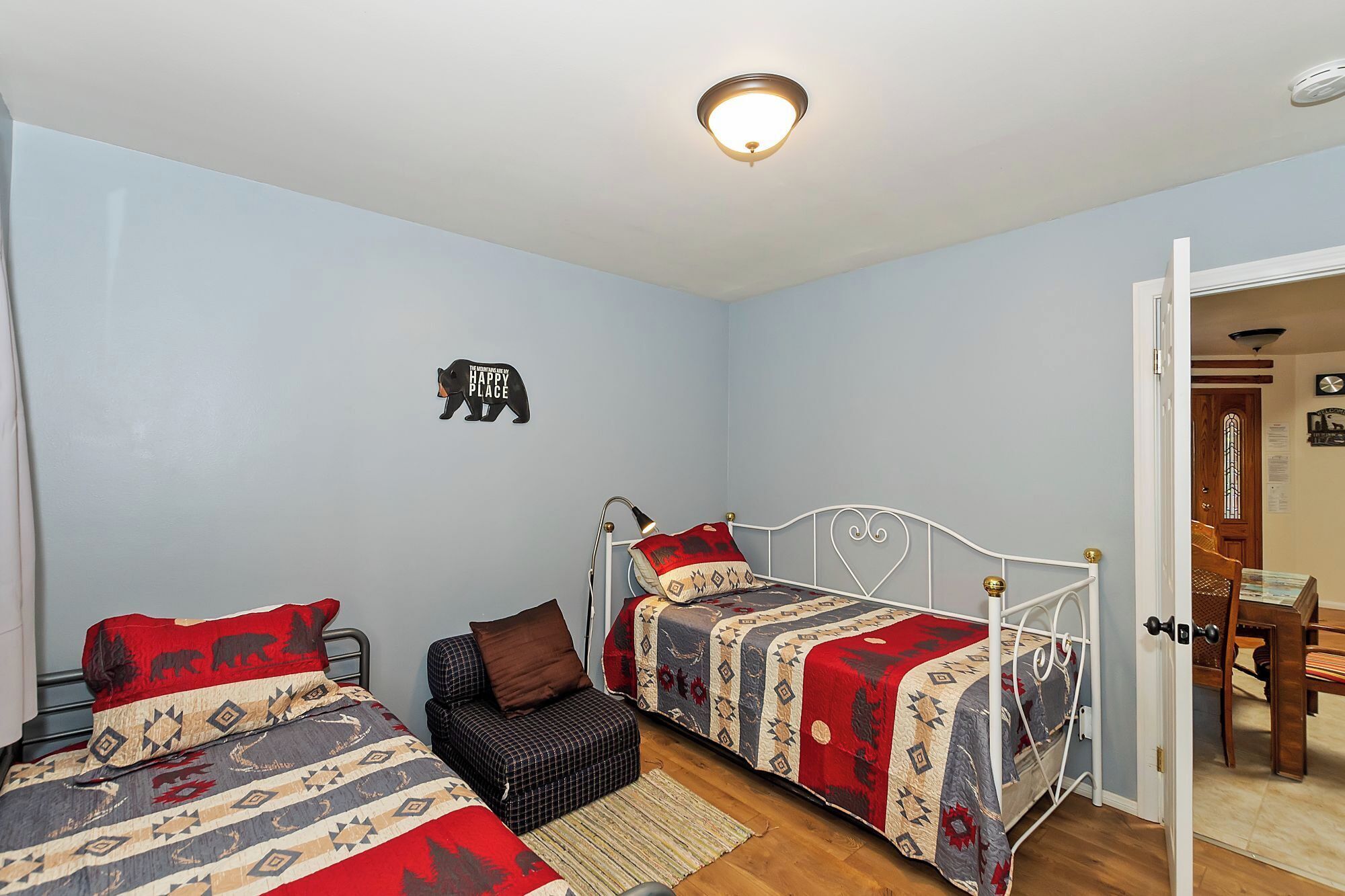 A bedroom with two beds, a wall-mounted light fixture, a door, and a small rug.