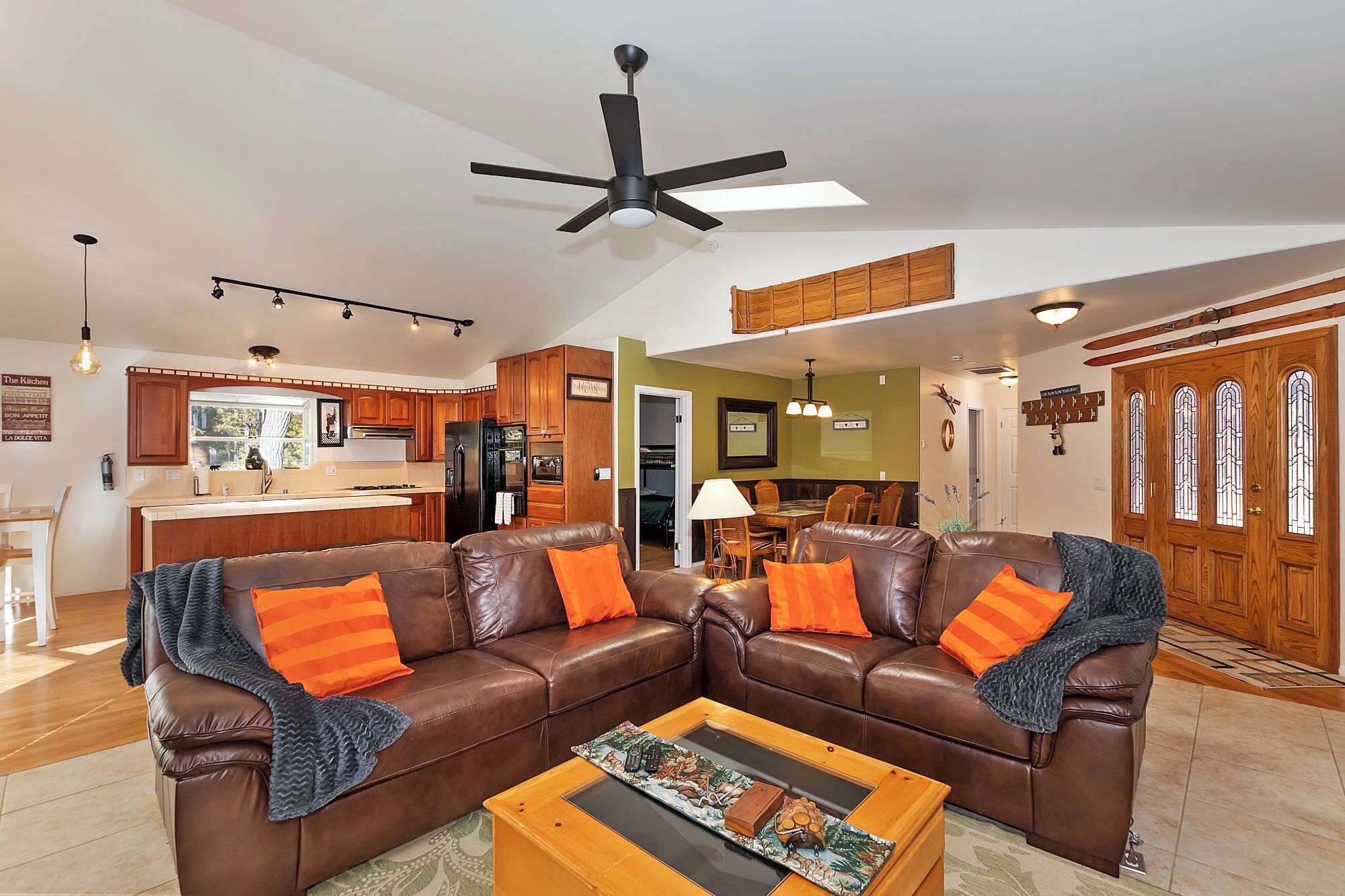A spacious living room with a brown leather sectional sofa, a coffee table with a board game, and a dining area with a wooden table and chairs.