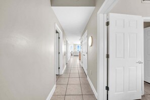 A hallway with white doors, a tiled floor, and a light fixture on the wall.