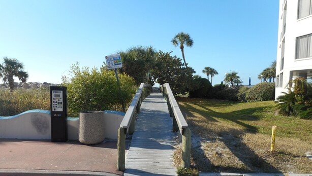 A pathway leading to a building with a palm tree and a signboard. -  Nice Condo directly on St Pete beach, walk to  restaurants/night life.  (St Pete Beach)