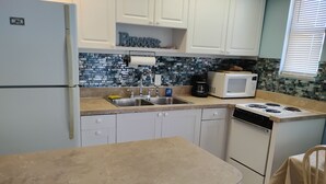 A kitchen with white cabinets, a microwave, a sink, and a stove. -  Nice Condo directly on St Pete beach, walk to  restaurants/night life.  (St Pete Beach)