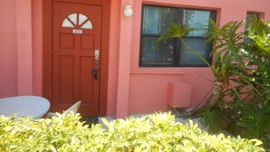 A red door with a number plate, a window with blinds, and a small plant in the foreground. -  Nice Condo directly on St Pete beach, walk to  restaurants/night life.  (St Pete Beach)