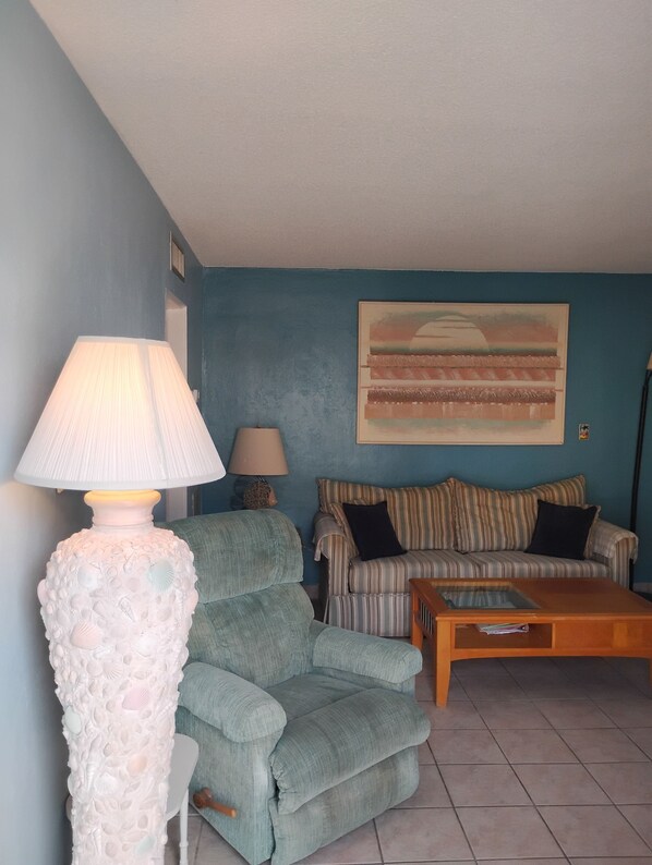 A living room with a blue wall, a striped sofa, a green armchair, a wooden coffee table, and a decorative lamp.