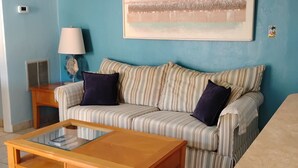 A living room with a striped sofa, a wooden coffee table, a lamp, and a painting on the wall. -  Nice Condo directly on St Pete beach, walk to  restaurants/night life.  (St Pete Beach)