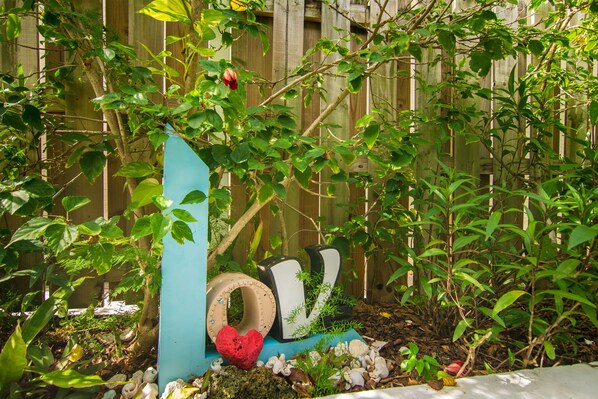 Un jardín con valla de madera, diversas plantas y elementos decorativos, incluyendo un objeto con forma de corazón y letras que deletrean 'LOVE'.