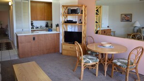 A compact kitchen with wooden cabinets, a built-in TV, and a dining area with wicker chairs and a table.