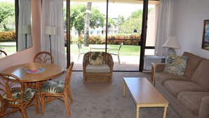 A living room with a dining table, chairs, a sofa, and a window with a view of greenery and buildings.
