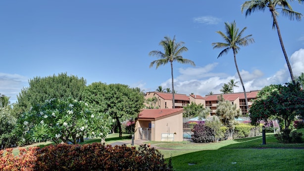 A hotel with a red-roofed building, palm trees, and a well-maintained garden.