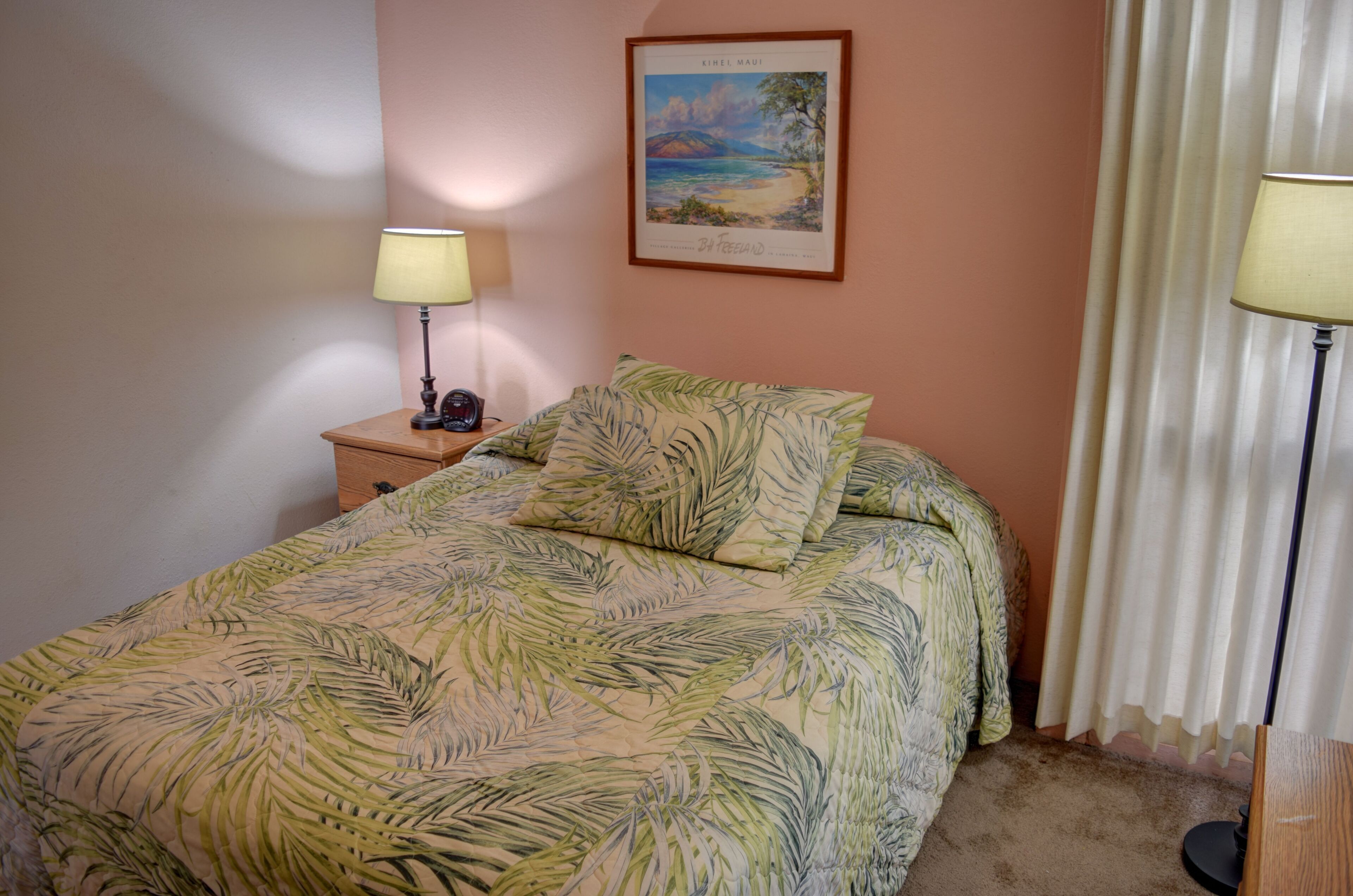 Une chambre à coucher avec un lit, une table de chevet, une lampe, un tableau encadré au mur et une fenêtre avec des rideaux.