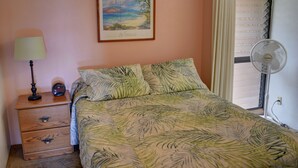 A bedroom with a bed, a nightstand, a lamp, a framed picture on the wall, and a window with blinds.