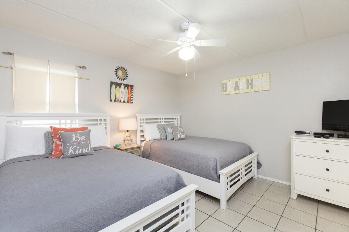A bedroom with two beds, a ceiling fan, a TV, and a dresser.
