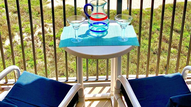 Een balkon met een tafel, twee stoelen en uitzicht op het strand.