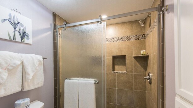 A bathroom with a shower, toilet, and towel rack. - ESCAPE to Bright Top Floor Beachfront Condo in Perfect Location (South Padre Island)