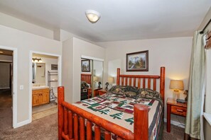 A bedroom with a wooden bed frame, a quilt, a bedside table with a lamp, and a window with curtains. - Luxury Town Home! Walk Summit! Hot Tub! Flat Fenced Yard! Foosball! (Big Bear Lake)