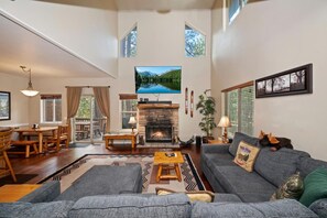 A spacious living room with a fireplace, a television mounted above it, and a large window with a scenic view.