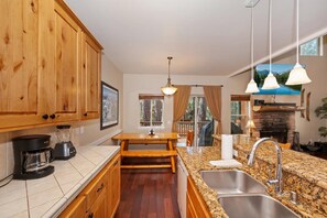 A kitchen with wooden cabinets, a granite countertop, a coffee maker, and a stone fireplace. - Luxury Town Home! Walk Summit! Hot Tub! Flat Fenced Yard! Foosball! (Big Bear Lake)