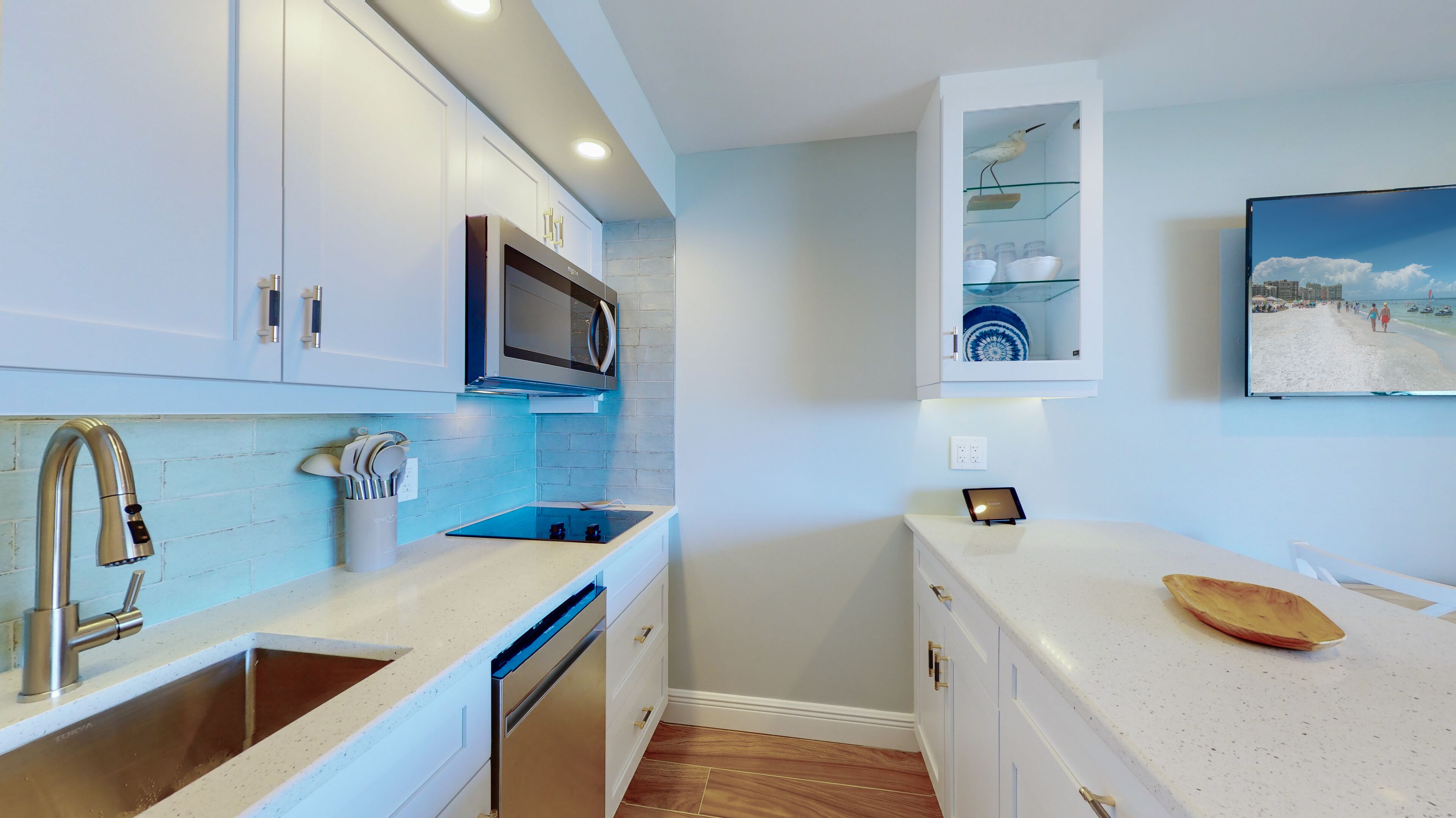 A modern kitchen with a built-in microwave, a sink with a modern faucet, and a countertop with a tablet and a wooden bowl.