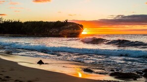 A beach with waves, a sunset, and a cliff.