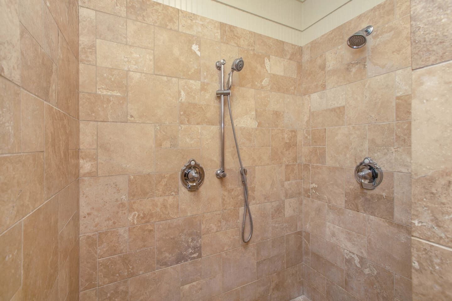 Une douche équipée d’un pommeau de douche à main et de deux robinets fixés au mur.