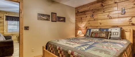 A cozy cabin-style room with a wooden headboard, a quilted bedspread, and a ceiling fan.