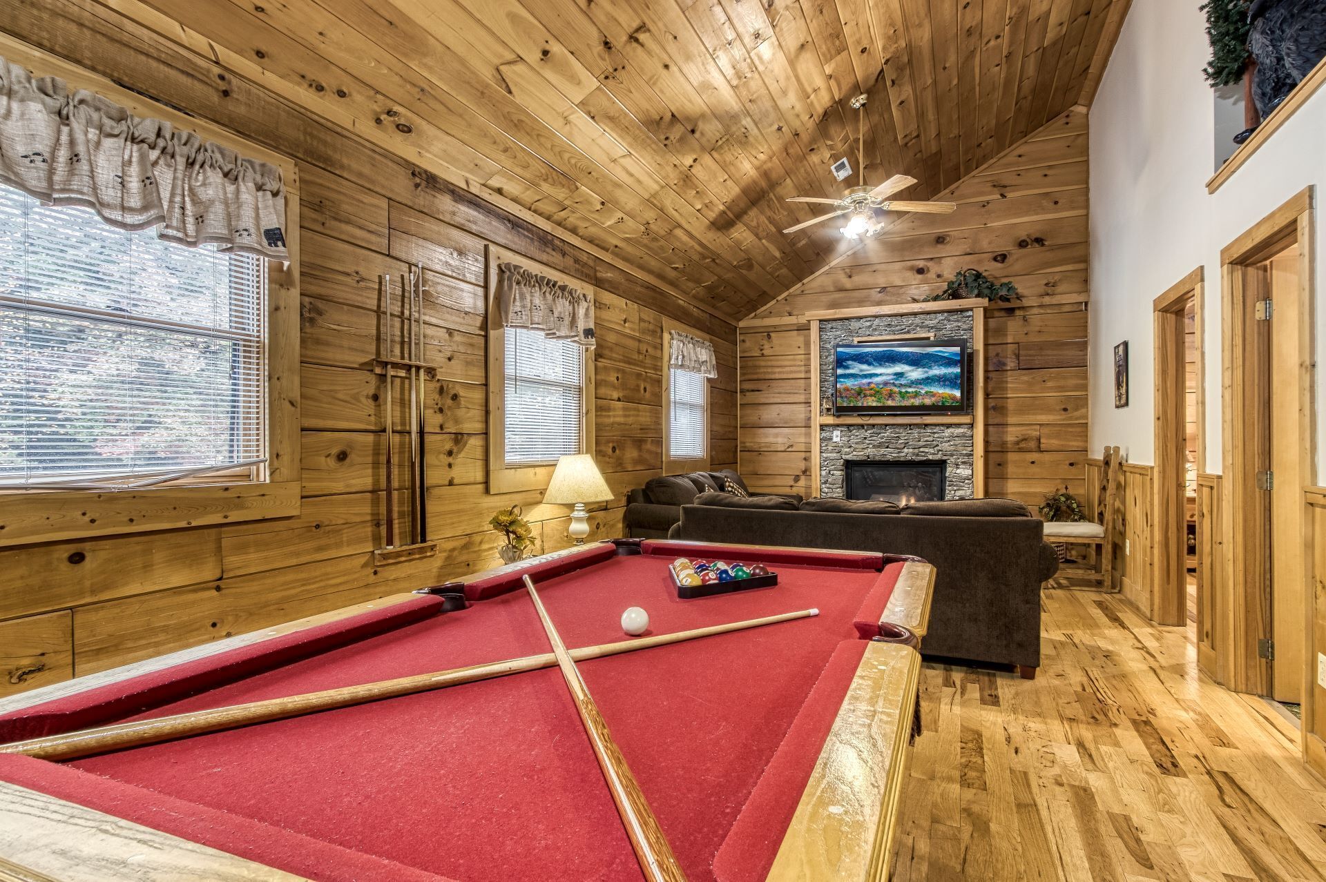 A cozy room with a pool table, wooden walls, a fireplace, and a ceiling fan.