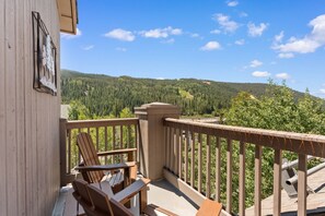 Eine Holzterrasse mit zwei Adirondack-Stühlen und Blick auf einen bewaldeten Bergrücken.
