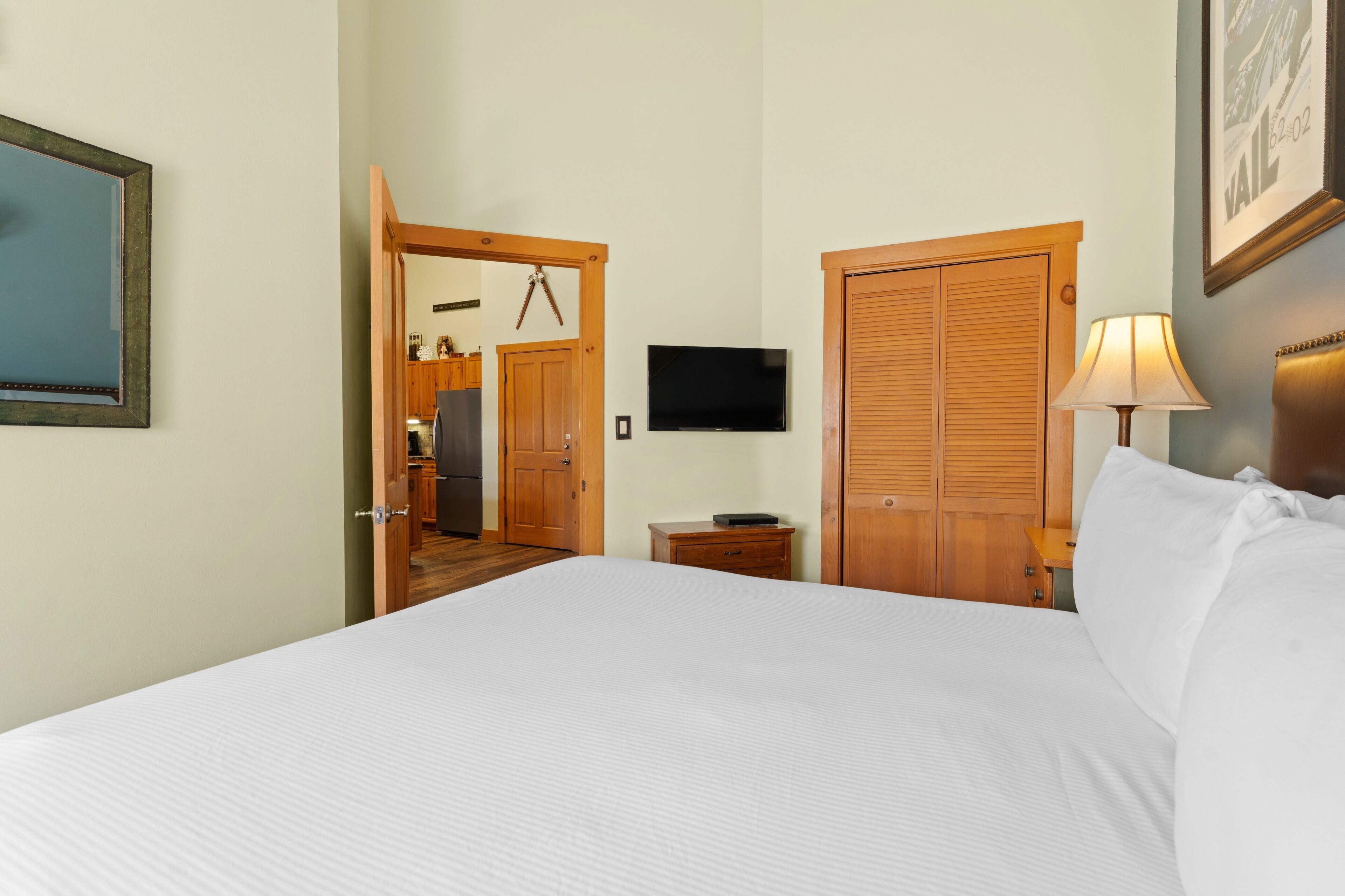 Una habitación de hotel con una cama, televisión, escritorio con lámpara y armario.