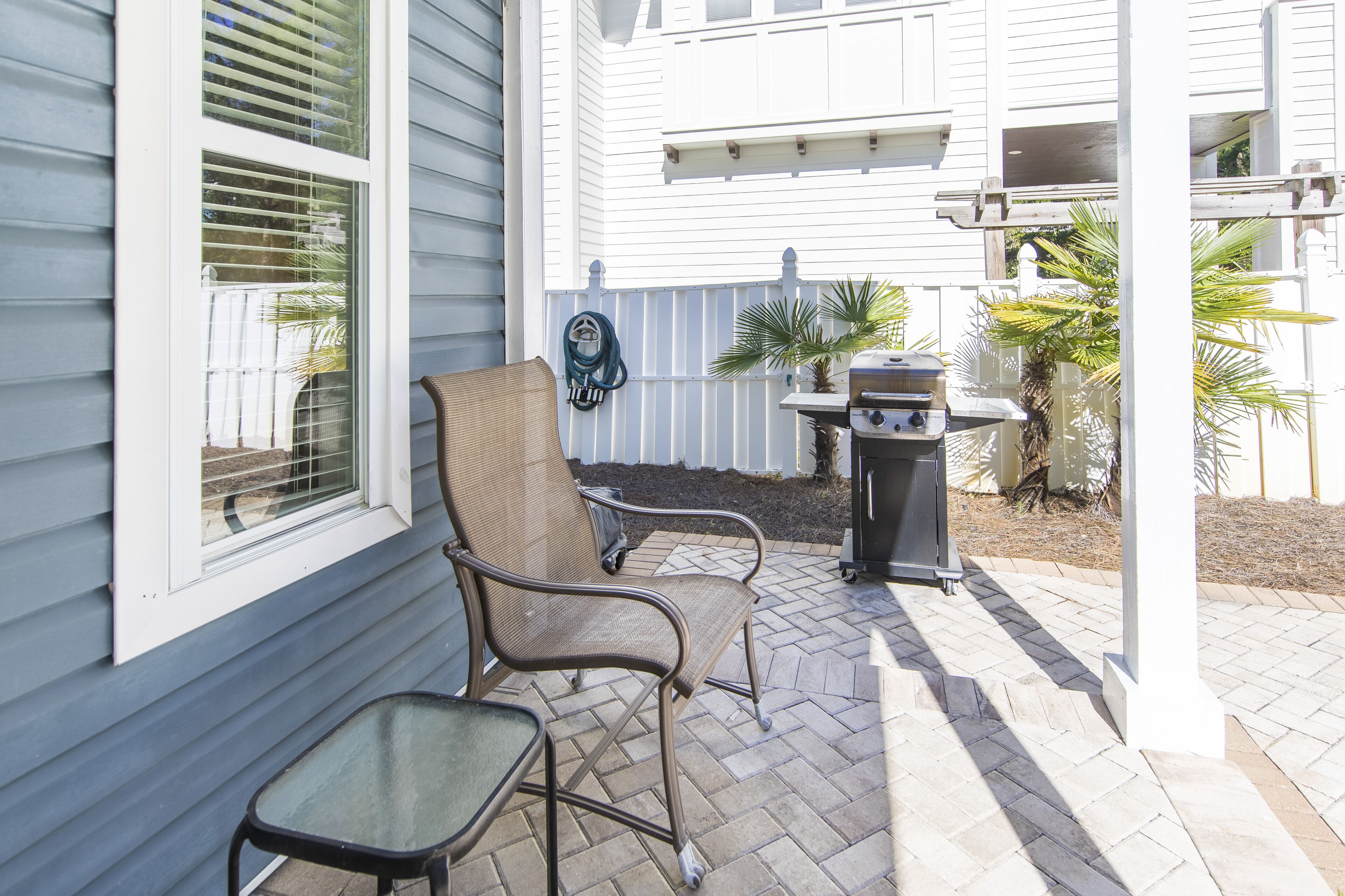 A patio with two chairs, a grill, and a hose.