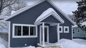 A single-story house with a dark siding exterior, a white front door, and a small porch area.