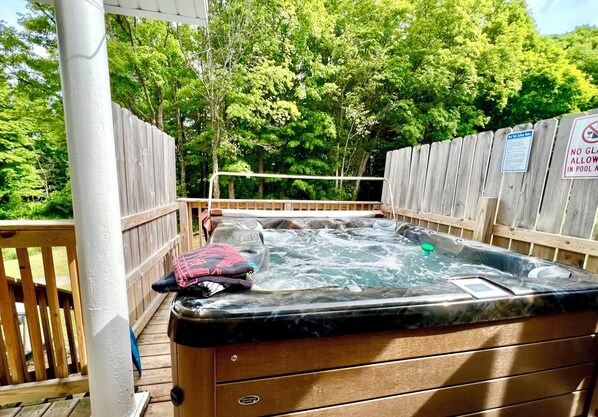 Un bain à remous sur une terrasse en bois, avec une clôture en bois et des arbres en arrière-plan.