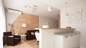 Un salon moderne avec un mur en briques, un espace cuisine aux couleurs claires et une table à manger.
