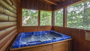 A wooden cabin with a hot tub, large windows, and a view of the forest. - ER65 - Eagles Point - Great location. Close to all the action! (Pigeon Forge)