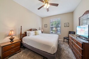 Ein Schlafzimmer mit Bett, Nachttisch, Kommode, Deckenventilator und einem Fenster mit Jalousien.