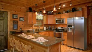 Una cocina de estilo cabaña con encimeras de madera, una isla central, taburetes de bar, refrigerador, microondas y pileta.