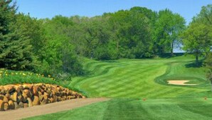 Un campo de golf con un fairway bien cuidado, búnkeres de arena y un muro de contención de piedra.