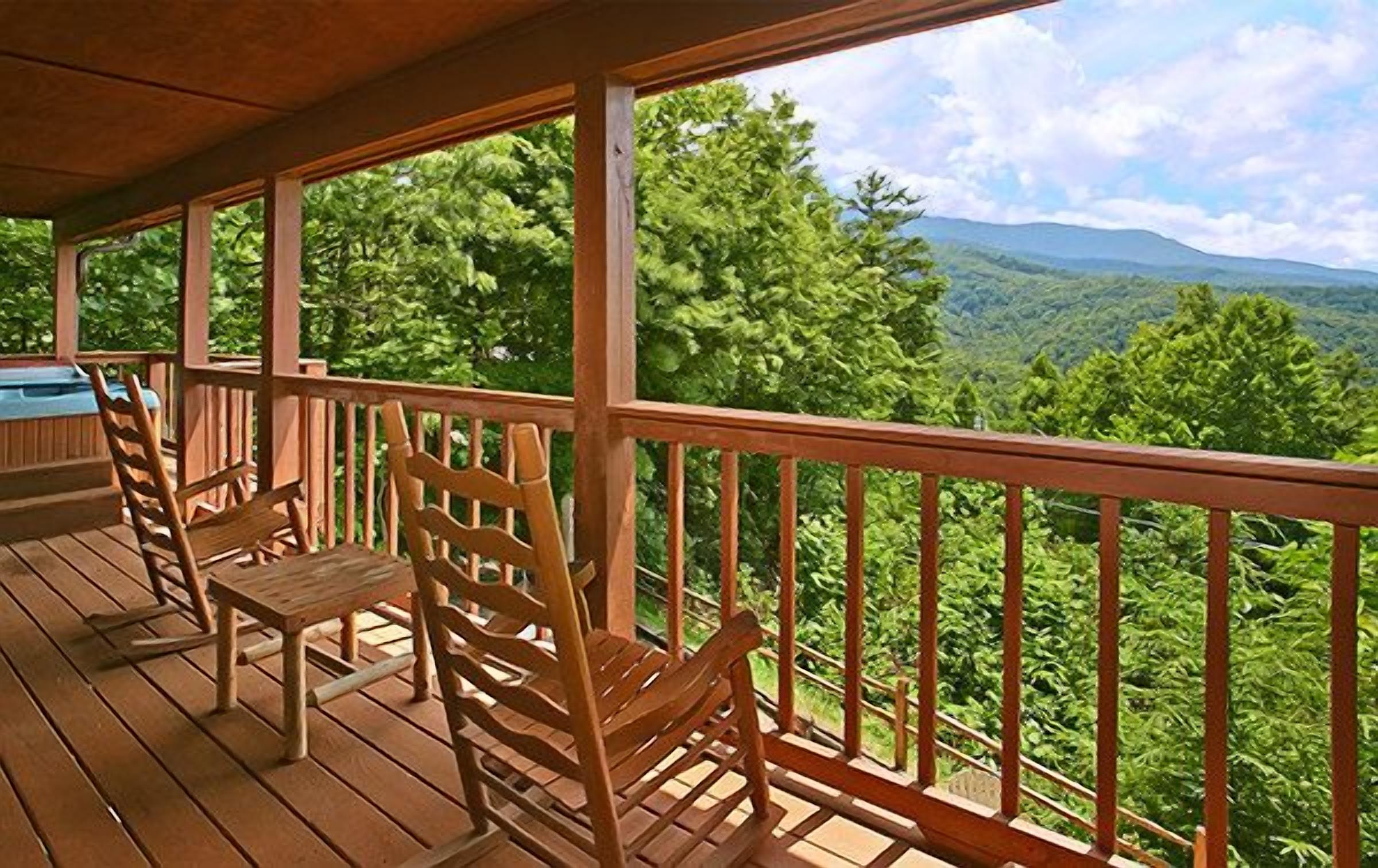 Una terraza de madera con sillas y vistas a una cadena montañosa boscosa.