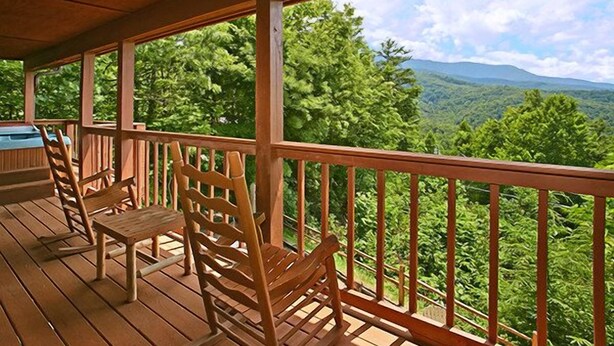 A wooden deck with chairs and a view of a forested mountain range.